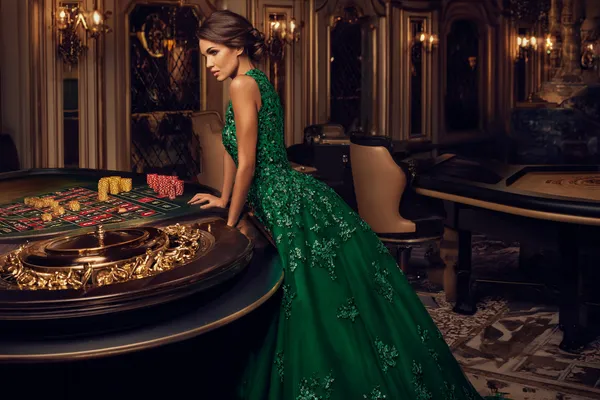 A woman in a luxurious green gown next to an ornate roulette wheel, capturing the upscale casino mood of FFBETT.